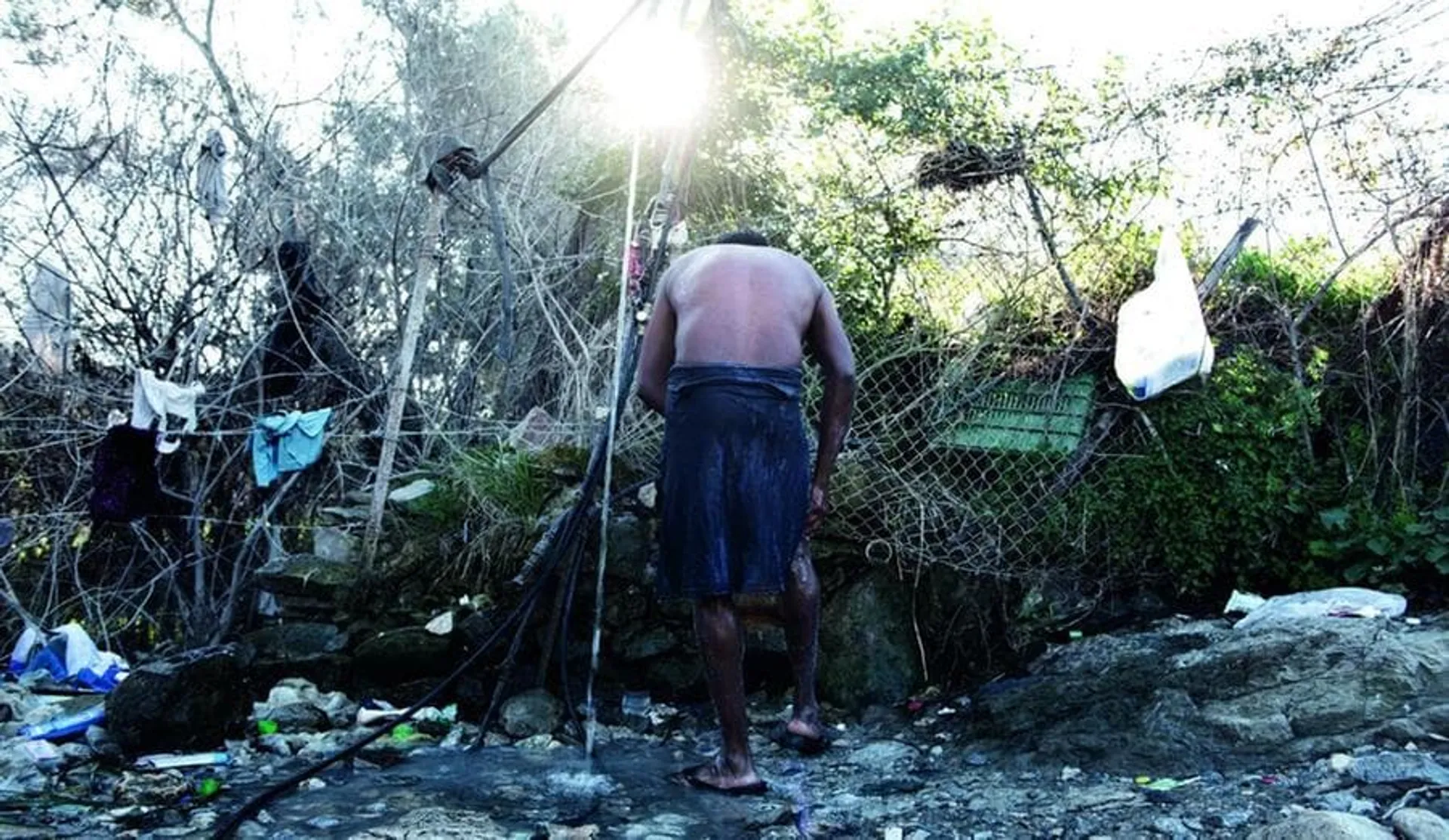 Greece, Lesvos: Un migrante bengalese si lava tra i cespugli grazie a un tubo messo a disposizione da un agricoltore locale. Alessio Romenzi