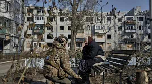 Una donna anziana con un militare, circondati da edifici distrutti a Pokrovsk