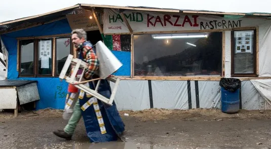 A migrant walks past a makeshift restaurant in the so-called "Jungle" migrant camp in Calais, on February 23, 2016.
A French court said on February 23, 2016 it was delaying its ruling on the demolition of half of the refugee camp in Calais known as the "Jungle", just hours before a deadline for residents to be evacuated. Emotions were running high in the "Jungle" on the outskirts of the northern port city of Calais, where many residents had refused to leave despite a 1900 GMT deadline to vacate the southern half of the camp. Local authorities say a total of 3,700 people are living in Jungle, and between 800 and 1,000 will be affected by the eviction. / AFP / DENIS CHARLET