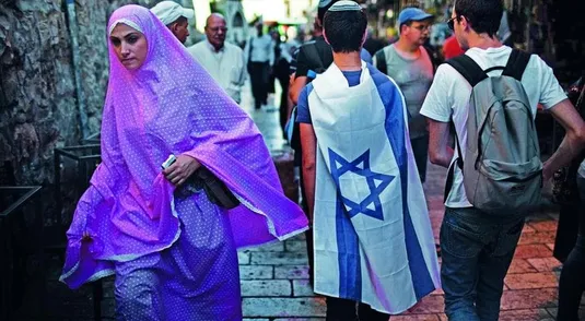 A Palestinian woman walks past Israelis marching in the old city of Jerusalem on June 1, 2011 during the Jerusalem Day parade in the city's mainly Arab eastern sector to celebrate its capture 44 years ago, during the Six Day War. AFP PHOTO /MENAHEM KAHANA (Photo credit should read MENAHEM KAHANA/AFP/Getty Images)