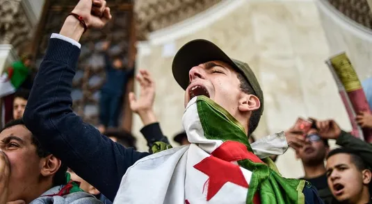 TOPSHOT - Algerian students shout slogans as they demonstrate with national flags outside La Grande Poste (main post office) in the centre of the capital Algiers on March 10, 2019 against ailing Algerian President Abdelaziz Bouteflika's bid for a fifth term. (Photo by RYAD KRAMDI / AFP)        (Photo credit should read RYAD KRAMDI/AFP/Getty Images)